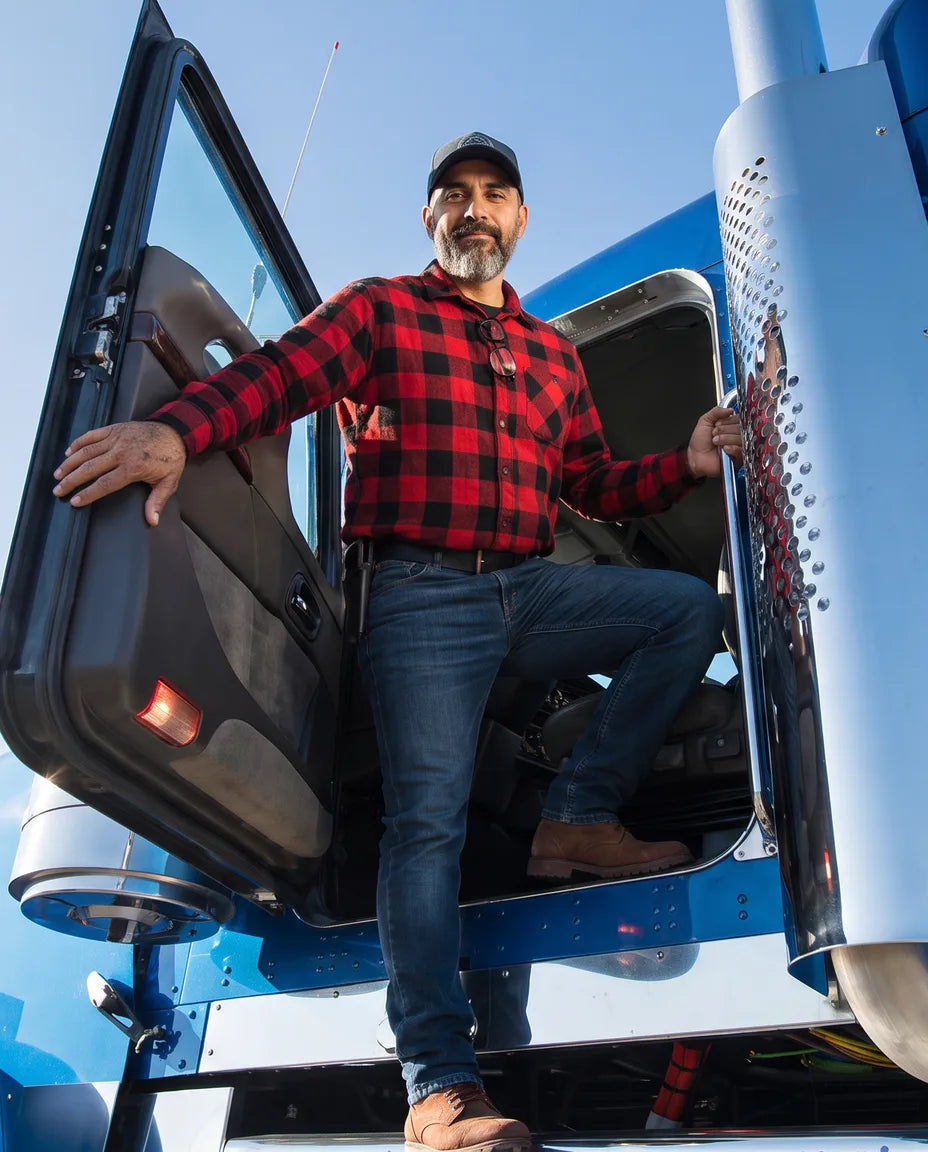 A long-haul driver standing in the open door of his truck cab